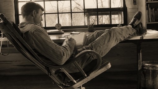 Wendell Berry reading in a chair beside a window